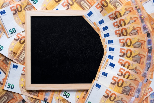 Black clarkboard as a frame on a background of money and a fan of euros from above flat lay copy