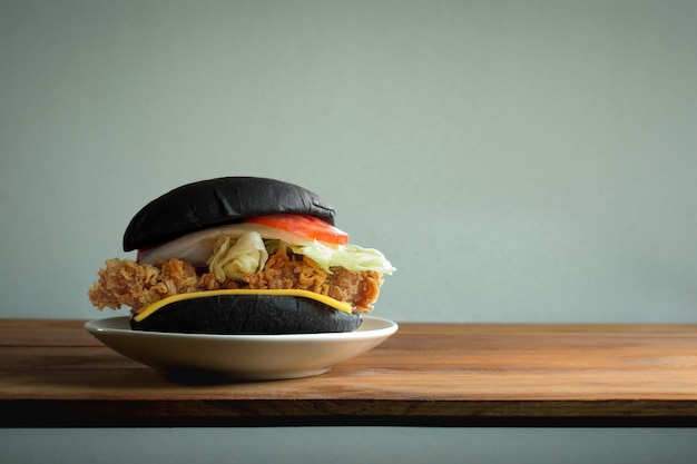 Photo black classic chicken burger on wood table with copy space and white wall background.