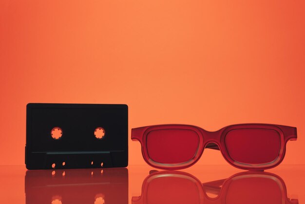 Photo black classic magnetic cassette tape and red glasses on a glass table beautiful coral orange backgr
