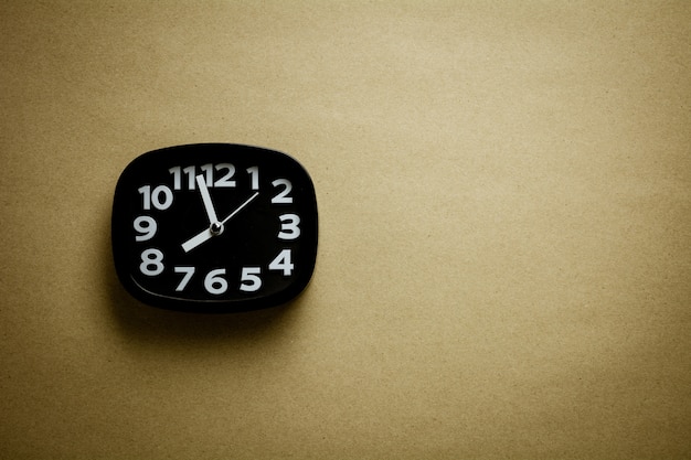 Black clock on brown recycled paper background.