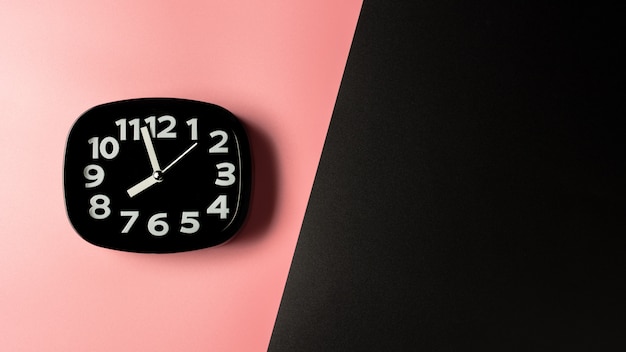 Black clock on pink and black background.