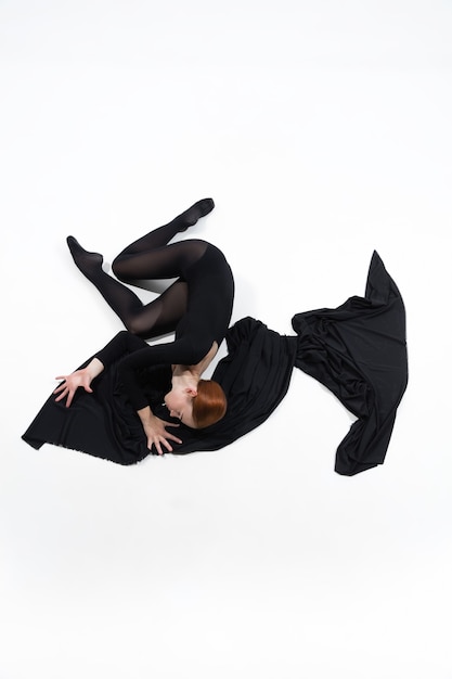 Black cloth. Young and graceful ballet dancer in minimal black style isolated on white studio background. Art, motion, action, flexibility, inspiration concept. Flexible caucasian ballet dancer.