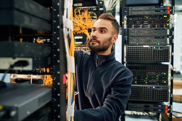 黒い服を着た若者はサーバールームでインターネット機器とワイヤーを操作しています