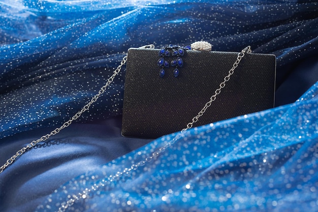 Black clutch with jewelry on background blue cloth