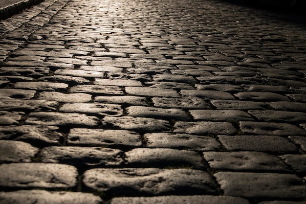 Black cobbled stone road background with reflection of light seen on the road