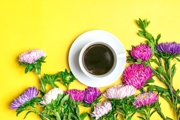 Black coffee americano in white cup and flowers asters on yellow background Flat lay