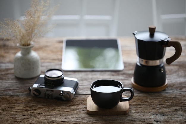 Black coffee cup and moka pot with camera and tablet on wooden table