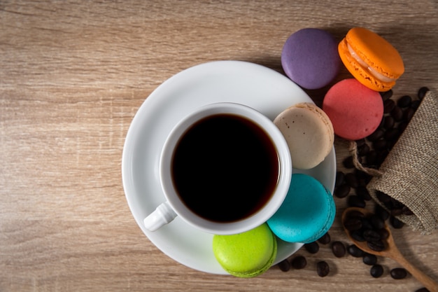 Foto caffè nero in una tazza con chicchi di caffè e amaretti sul fondo della tavola in legno