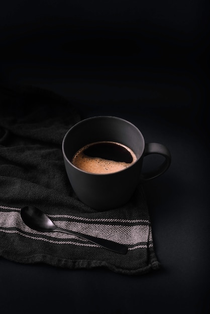 Black coffee cup with coffee foam and black spoon, on black and white cloth