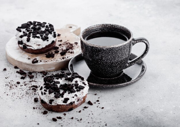 Black coffee cup with saucer and doughnuts with black cookies on stone kitchen table.