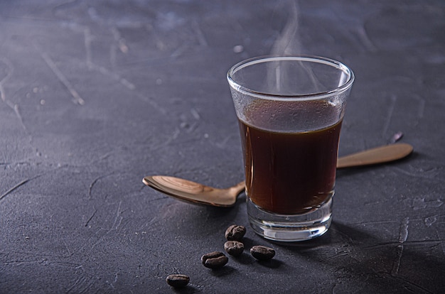 Caffè nero su superficie scura con chicchi di caffè e cucchiaino.