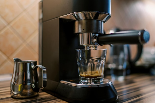 Photo black coffee drips into a glass on the tray of a carob coffee machine on a table