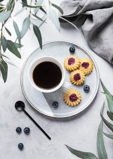 Black coffee espresso in a cup with homemade berry cookies and blueberries on a light background