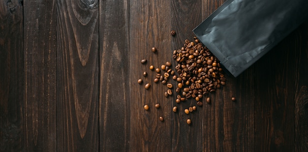 Black coffee foil packaging bag and spilled beans on wooden table