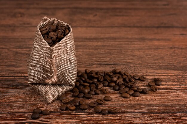 Black coffee foil packaging bag on wooden table top view. Spilled beans flat lay concept. Room for text.