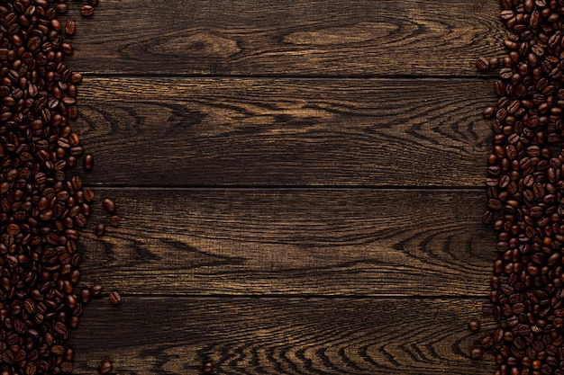 I chicchi di caffè nero giacciono sul fondo astratto della tavola di legno marrone con struttura del bordo di legno e roaste