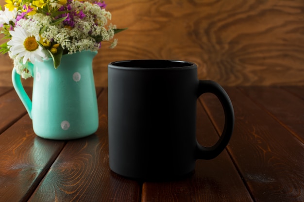 Photo black coffee mug with wildflowers in mint green vase