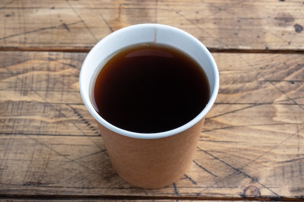 Black coffee in a paper cup on a wooden background. flat lay copy space, top view.