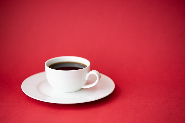 Black coffee in a small white coffee cup on a red background