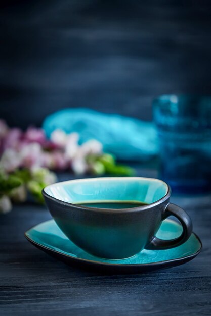 Black coffee in a turquoise cup and flowers on a black wooden background