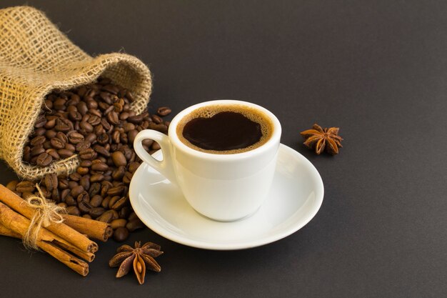 Черный кофе в белой чашке, корица и кофейные зерна на темном фоне
