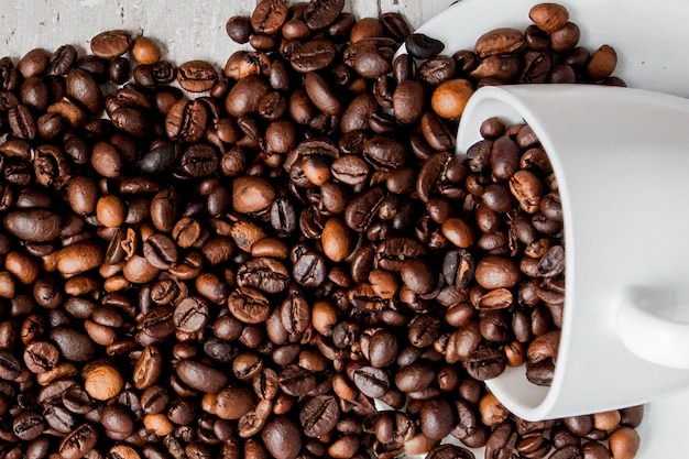 Black coffee in white cup and coffee beans on light wooden background. Top view, space for text.