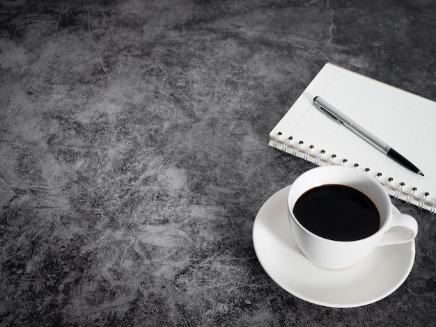 Black coffee white cup with notebook on dark floor table copy space top view