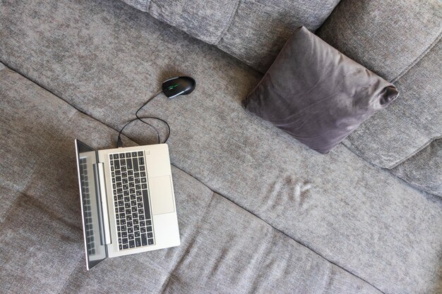 Black computer mouse and a steel thin laptop on the surface of a gray loft sofa the concept of remot