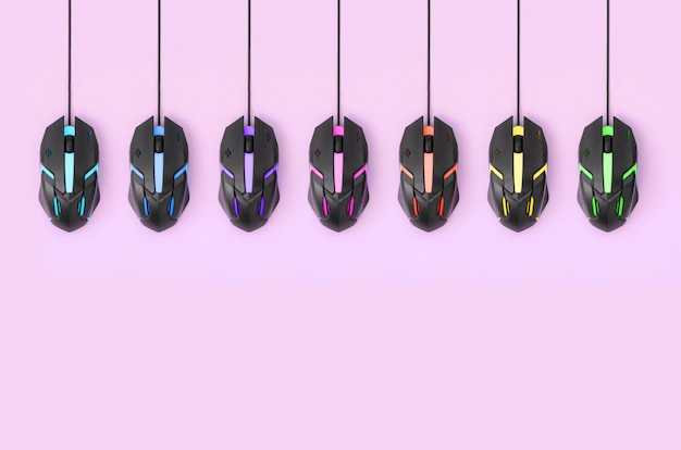 Black computer mouses hang on pastel pink background