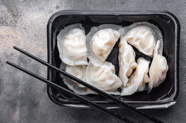 A black container of dumplings with chopsticks and a black plastic fork