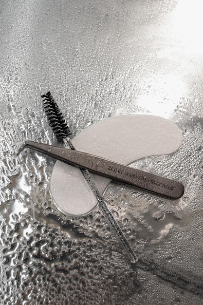 Фото Черная косметическая щетка для бровей и ресниц, пинцет и пластыри для бровей лежат на мокром столе