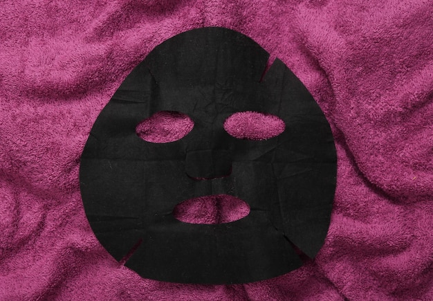 Foto maschera di pulizia cosmetica nera su asciugamano rosa cura della pelle terapia anti-invecchiamento vista superiore