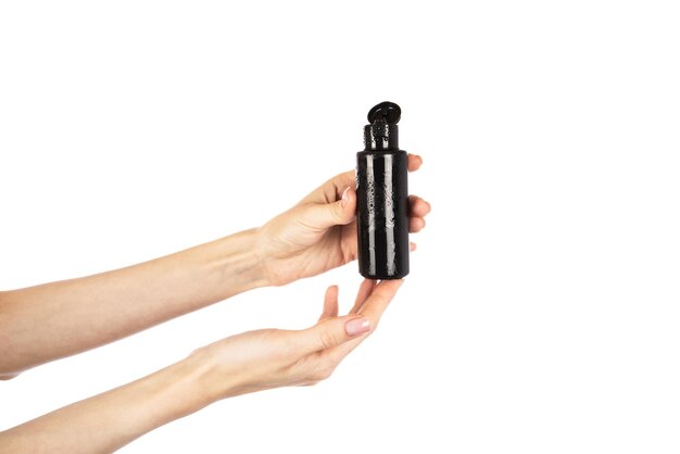 Черная косметическая бутылка с откидной крышкой в женских руках на белом фоне