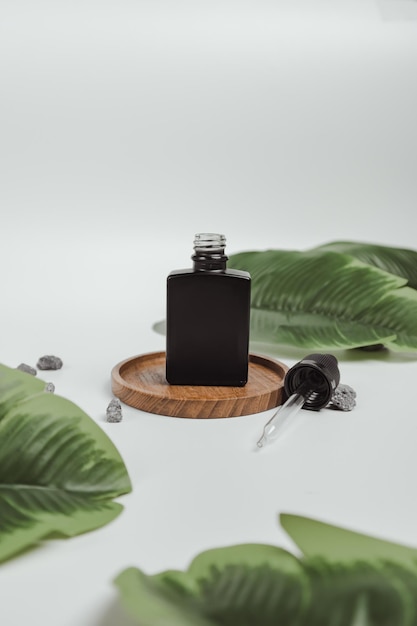 Photo black cosmetic serum bottle mock up with white background and leaves