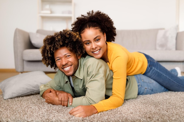 Black couple embracing on floor smiling to camera at home