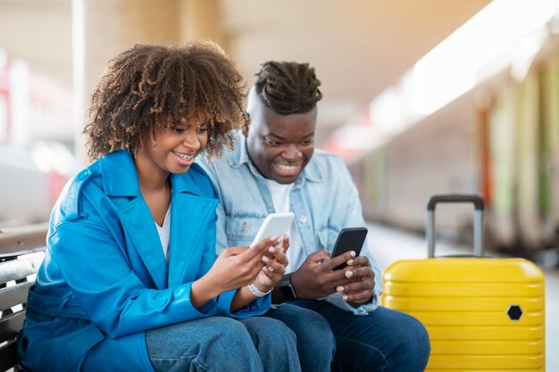 Black couple playing games on smartphones while waiting train at railway station