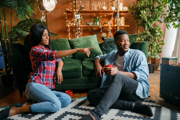 Black couple sitting on floor and drinks coffee