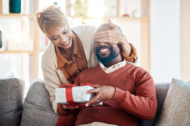 Black couple surprise gift and Christmas present in festive summer season from wife with love happiness and holiday celebration Black woman happy man and smile the living room home sofa together