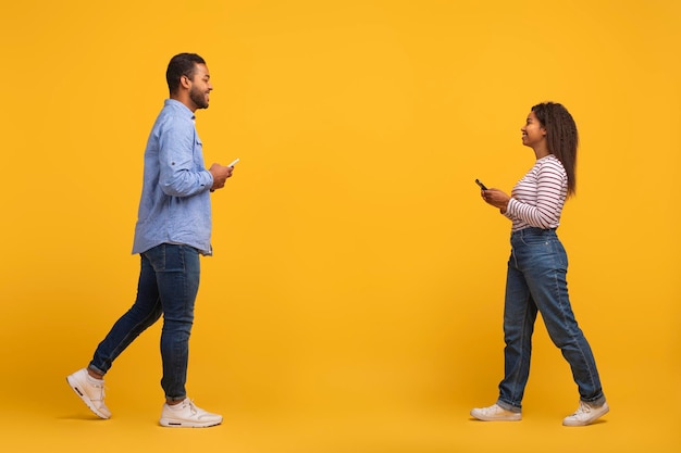 Photo black couple with mobile phones in hands walking past each other