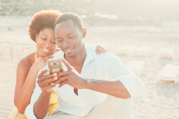 Black couple young man and woman enjoy together connection technology using mobile phone and app happy modern people writing on smartphone in outdoor leisure activity together smiling and having fun