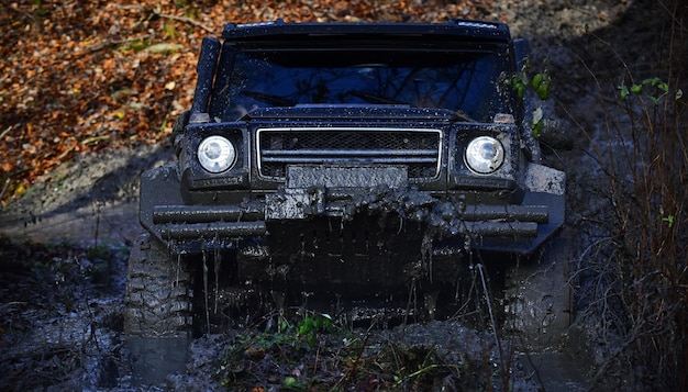 Black crossover driving through dirt with nature on background.