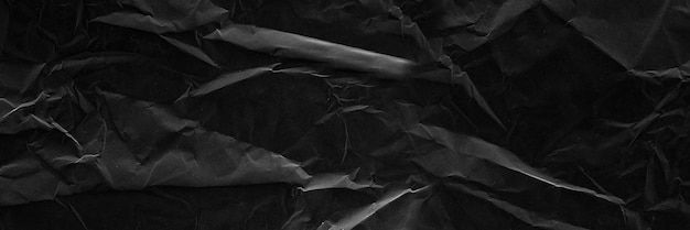 Black crumpled paper texture with folds Black wallpaper background