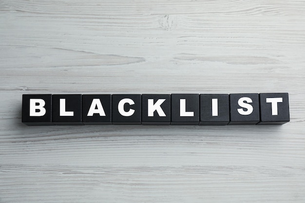 Photo black cubes with word blacklist on white wooden background flat lay