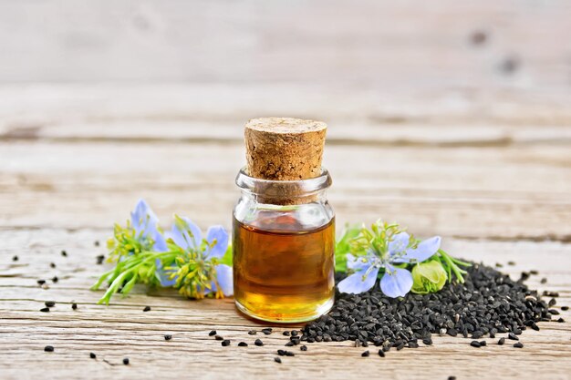 black cumin oil in bottle, seeds and twigs of seeds with blue flowers and leaves of kalingi on board