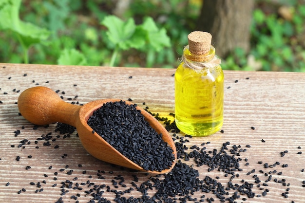 Photo black cumin seeds and essential oil with bowl and wooden shovel or spoon nigella sativa