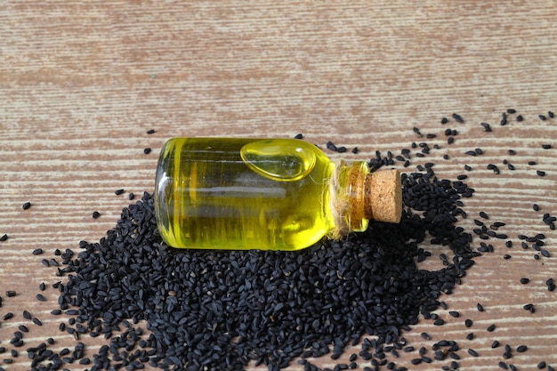 Photo black cumin seeds and essential oil with bowl and wooden shovel or spoon nigella sativa