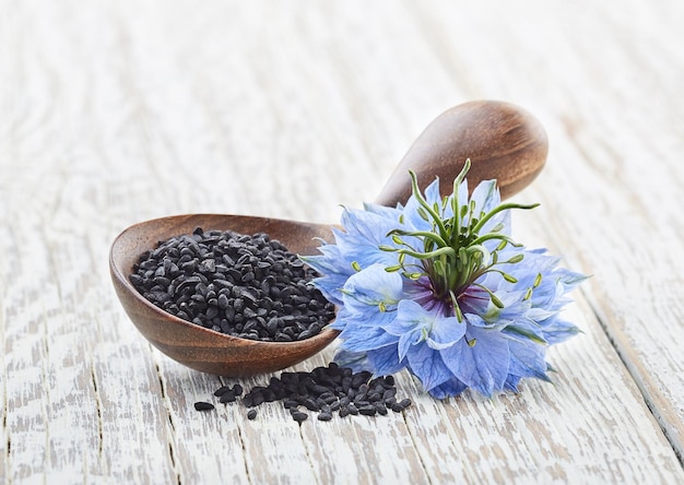 Black cumin seeds with flower on old white wooden background