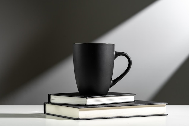 Black cup on books in sunlight on gray background