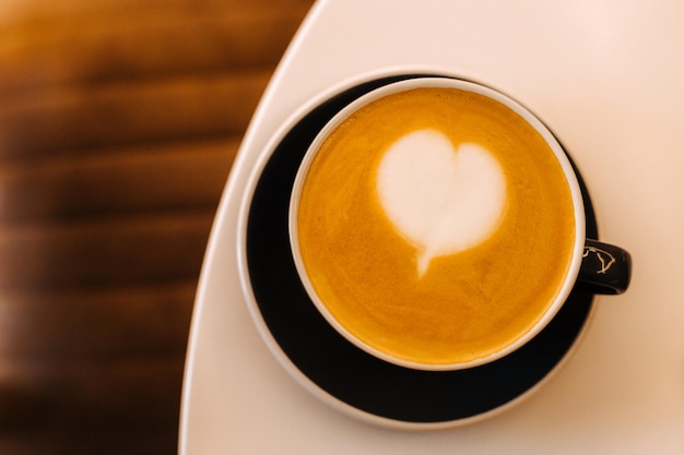 Black cup of cappuccino on saucer with latte art on white table background