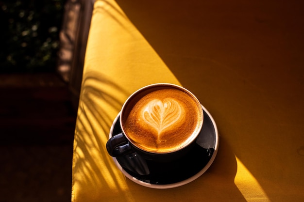 Black cup of cappuccino with latte art on yellow sofa background